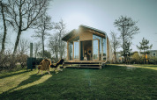 Wikkelhouse Bear naturhus i ferieland De Klepperstee, Holland, omgivet af grønne træer og åbent græsareal.