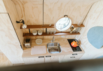 Moderne, compacte keuken met houten panelen, wasbak, planken en oranje waterkoker in Wikkelhouse Bear.