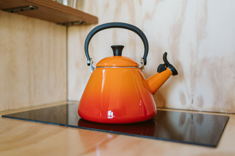 Een oranje theeketel op een kookplaat in Wikkelhouse Bear, een natuurhuisje in De Klepperstee, Nederland.