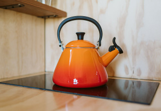 Een oranje waterkoker op een fornuis in Wikkelhouse Bear, een natuurhuisje in De Klepperstee, Nederland.