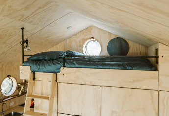 Lit en mezzanine avec draps verts dans Wikkelhouse Bear, maison nature du parc De Klepperstee, Pays-Bas.