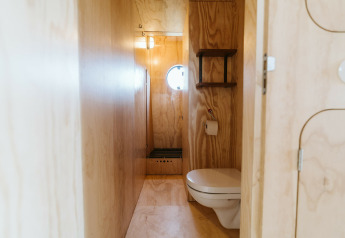 Baño minimalista con paredes de madera, inodoro flotante y ventana redonda en Wikkelhouse Bear, Países Bajos.