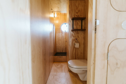 Baño minimalista con paredes de madera, inodoro flotante y ventana redonda en Wikkelhouse Bear, Países Bajos.
