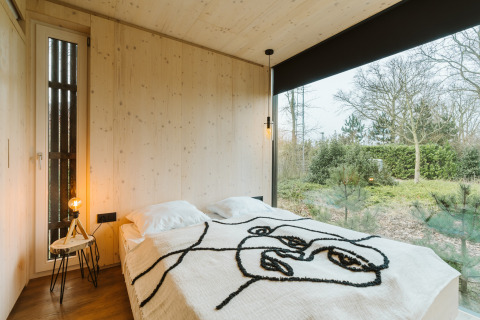 Moderne soveværelse i Ark Shelter ved De Klepperstee, Nederlandene, med store vinduer og naturudsigt.
