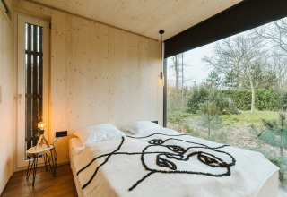 Moderne slaapkamer in Ark Shelter, De Klepperstee, Nederland, met groot raam en uitzicht op de natuur.