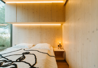 Moderne slaapkamer van hout met tweepersoonsbed, groot raam en sfeerverlichting in Ark Shelter, De Klepperstee.