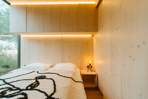 Moderne slaapkamer van hout met tweepersoonsbed, groot raam en sfeerverlichting in Ark Shelter, De Klepperstee.