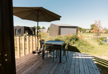 Holzterrasse mit Tisch, vier Stühlen und Sonnenschirm an einem Tiny House im De Klepperstee, Niederlande.