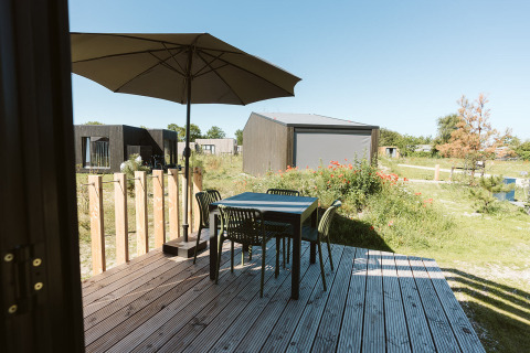 Terraza de madera con mesa, cuatro sillas y sombrilla junto a una tiny house en De Klepperstee, Países Bajos.