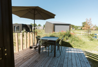 Houten terras met tafel, vier stoelen en parasol bij een tiny house op De Klepperstee, Nederland, zonnige dag.