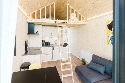 Lichte, moderne tiny house met een loft, kitchenette, ladder en bank op vakantiepark De Klepperstee in Nederland.