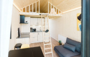 Lichte, moderne tiny house met een loft, kitchenette, ladder en bank op vakantiepark De Klepperstee in Nederland.