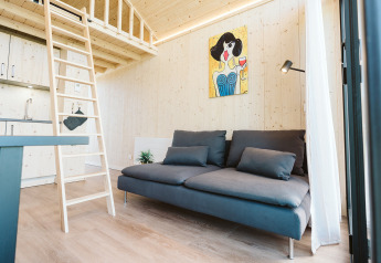Sala moderna y luminosa en una tiny house del Holiday park De Klepperstee, Países Bajos, con sofá y altillo.