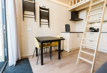 Interno di una tiny house a De Klepperstee, Paesi Bassi, con tavolo da pranzo, scala e arredo in legno.