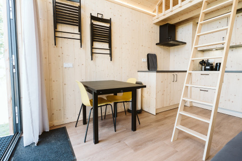 Interieur van een tiny house op De Klepperstee, Nederland, met eettafel, gele stoelen en houten ladder.