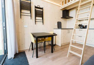 Interior de una tiny house en De Klepperstee, Países Bajos, con mesa, sillas, escalera y decoración de madera.