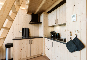 Modernes, kleines Holzküchen mit schwarzen Arbeitsplatten und Geräten unter einer Treppe im Ferienhaus.