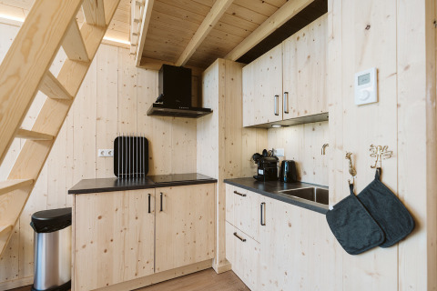 Pequeña cocina moderna de madera con encimeras negras y electrodomésticos bajo una escalera de casa.
