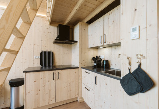 Moderne kleine houten keuken met zwarte werkbladen en apparaten onder een trap in een vakantiehuis.