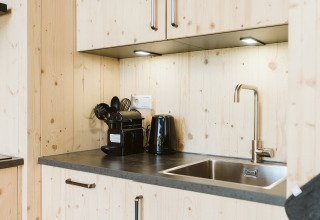 Petite cuisine moderne en bois avec évier, bouilloire, cafetière et ustensiles dans une maison de vacances.