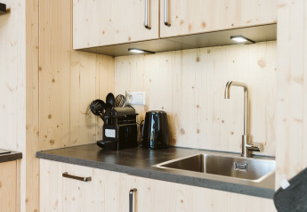 Angolo cottura moderno in legno con lavello, bollitore, macchina da caffè e utensili in una tiny house.
