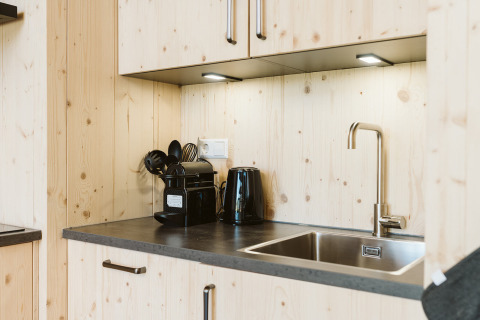 Pequeña cocina moderna de madera con fregadero, hervidor, cafetera y utensilios en una casa vacacional.