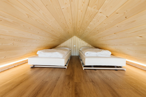 Dos camas individuales bajo un techo inclinado de madera en Stulp, una tiny house en De Klepperstee, Países Bajos.