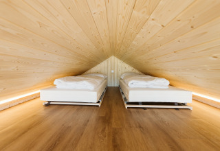 Dos camas individuales bajo un techo inclinado de madera en Stulp, una tiny house en De Klepperstee, Países Bajos.