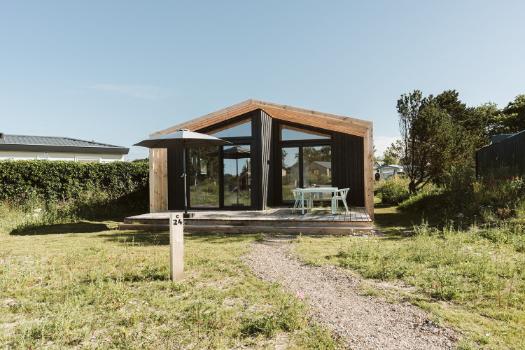 Een modern natuurhuisje met grote ramen en houten terras op vakantiepark De Klepperstee in Nederland.