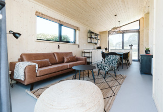 Moderne woonkamer met leren bank, groot raam en eethoek in een natuurhuis op De Klepperstee, Nederland.