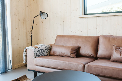 Salón moderno con sofá de cuero marrón, lámpara de pie y pared de madera en Barn, De Klepperstee, Países Bajos.