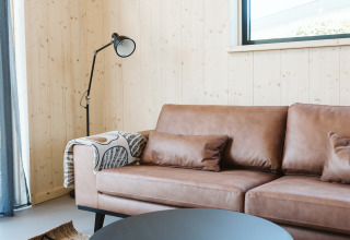 Moderne stue med lædersofa, stående lampe og lys trævæg i et naturhus på De Klepperstee i Holland.