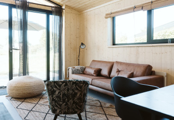 Lichte, moderne woonkamer met houten wanden, leren bank en grote ramen bij De Klepperstee, Nederland.