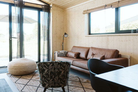 Salon lumineux et moderne avec murs en bois, canapé en cuir et grandes fenêtres à De Klepperstee, Pays-Bas.