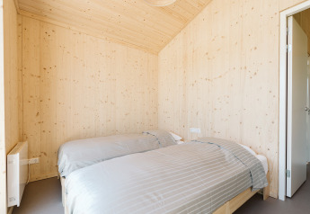 Slaapkamer met twee eenpersoonsbedden en lichte houten wanden in een natuurhuis op De Klepperstee, Nederland.