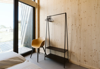 Modern, minimalist room with wooden walls, yellow chair, and clothes rack at De Klepperstee, Netherlands.