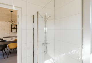 Moderne douche met witte tegels en zicht op eetruimte van een vakantiehuis in Nederland.