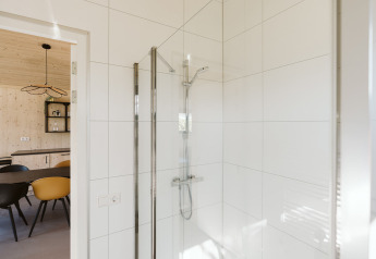Moderne douche met witte tegels in badkamer, doorkijk naar eetgedeelte in vakantiehuis in Nederland.
