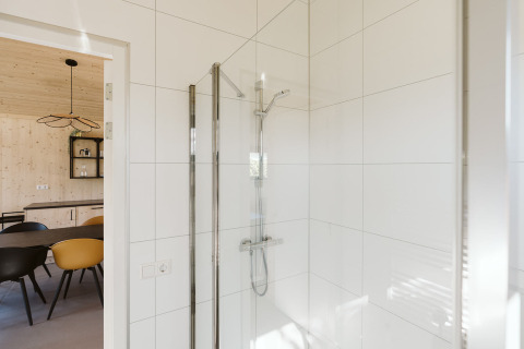 Douche moderne avec carrelage blanc dans la salle de bain, vue sur salle à manger d'une maison de vacances.