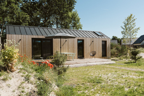 Modern wooden tiny house at De Klepperstee Holiday Park in the Netherlands, with terrace, garden, and chairs.