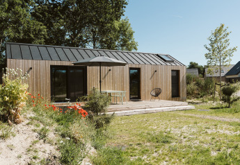 Modern wooden tiny house at De Klepperstee Holiday Park in the Netherlands, with terrace, garden, and chairs.