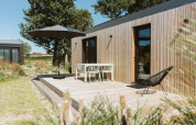 Terraza de madera junto a una tiny house en De Klepperstee, Países Bajos, con muebles de jardín y sombrilla.