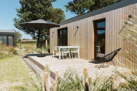 Houten terras van een tiny house in De Klepperstee, met tuinmeubilair en parasol onder een blauwe lucht.