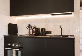 Cocina negra moderna con horno, fregadero y utensilios en la tiny house Punt de De Klepperstee, Países Bajos.