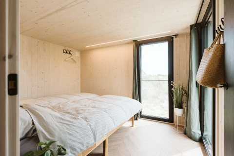 Bright bedroom in Punt tiny house at Holiday park De Klepperstee, Netherlands, with large windows.