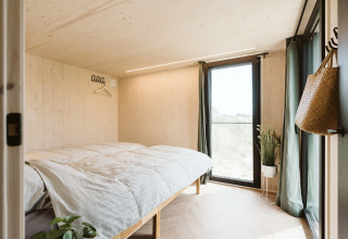Bright bedroom in Punt tiny house at Holiday park De Klepperstee, Netherlands, with large windows.