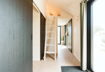 Interior de la tiny house Punt en Holiday park De Klepperstee, Países Bajos, con altillo y ventanas grandes.
