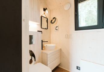 Bagno moderno in legno chiaro con lavabo tondo e finestra nera nella tiny house Punt, Olanda.