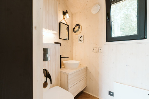 Moderne badeværelse i lyse træfarver med håndvask, rundt spejl og sort vindue i tiny house Punt.