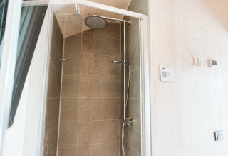 Shower in Punt tiny house at Holiday park De Klepperstee in the Netherlands, featuring tiled walls and rain shower.